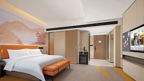 A hotel room with a large bed, an orange bench, a desk, and a television.
