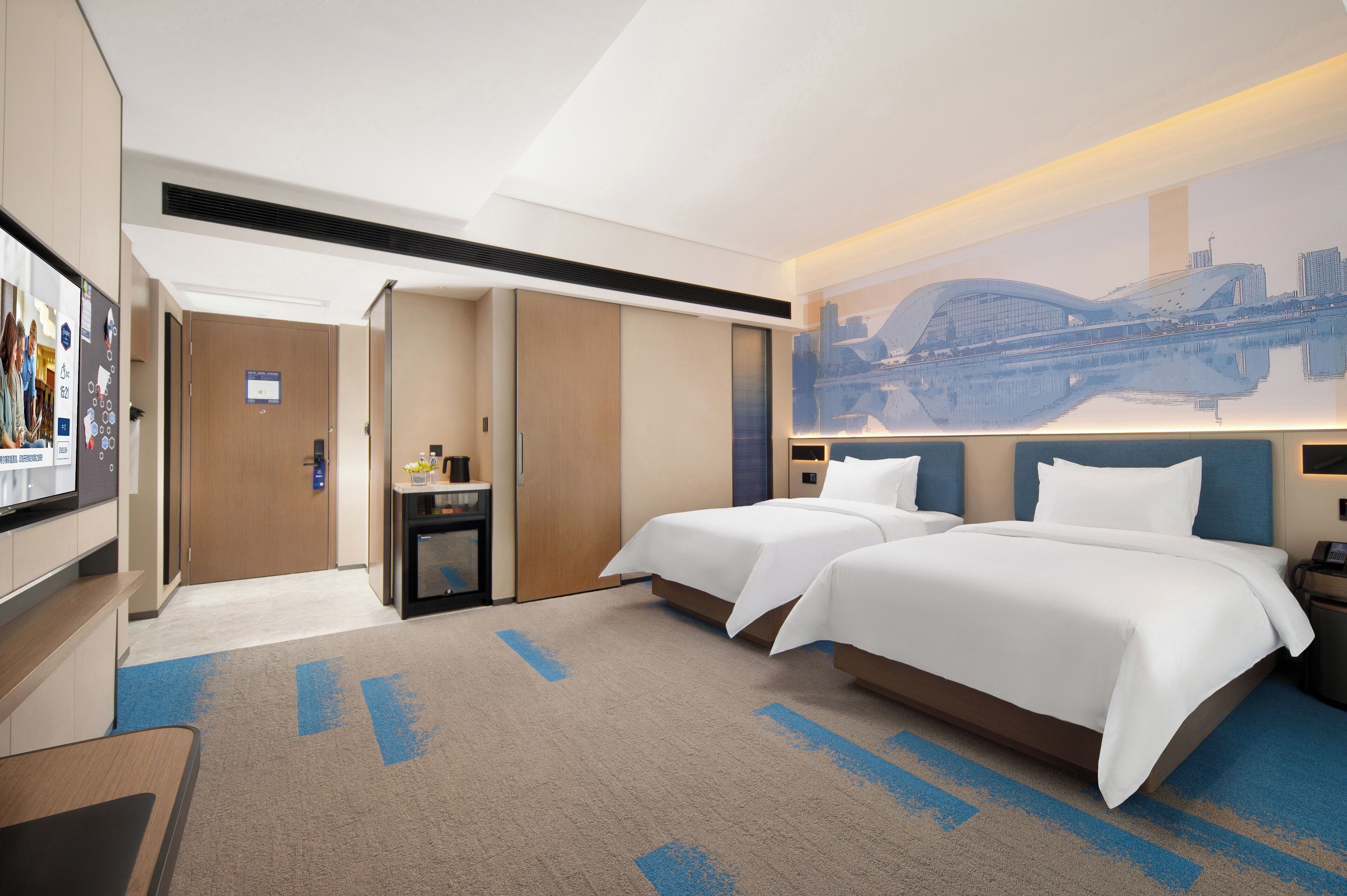 Habitación de hotel con dos camas, un escritorio, una silla, un televisor y un mural con vista a la ciudad.