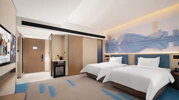 Een hotelkamer met twee bedden, een bureau, een stoel, een televisie en een muurschildering van een stadsgezicht.