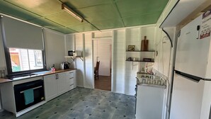 Kompakti keittiö, jossa on mikroaaltouuni, pesuallas ja jääkaappi. Siinä on ikkuna, josta tulee luonnonvaloa, ja ovi, joka johtaa toiseen huoneeseen.