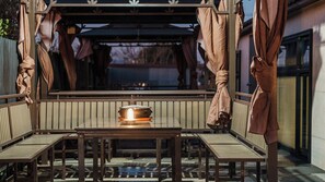 A covered outdoor seating area with a table and chairs, a fire feature, and a view of a building.