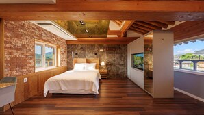 A bedroom with a brick wall, wooden ceiling, a bed, a nightstand, a TV, and a balcony with a view. - Hanok Pension Wanggyeong (Gyeongju)
