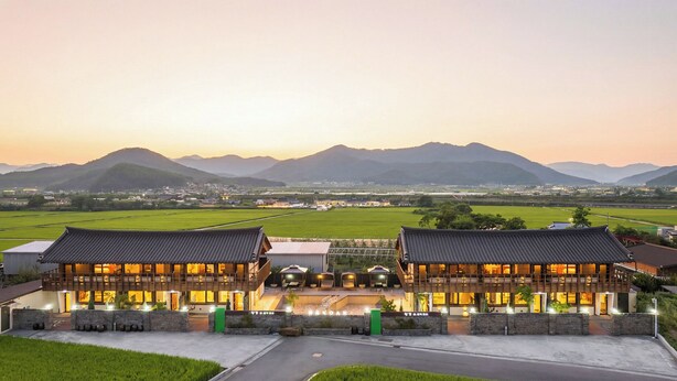 A traditional building with a modern extension, featuring a large open entrance and a view of surrounding fields and mountains. - Hanok Pension Wanggyeong (Gyeongju)
