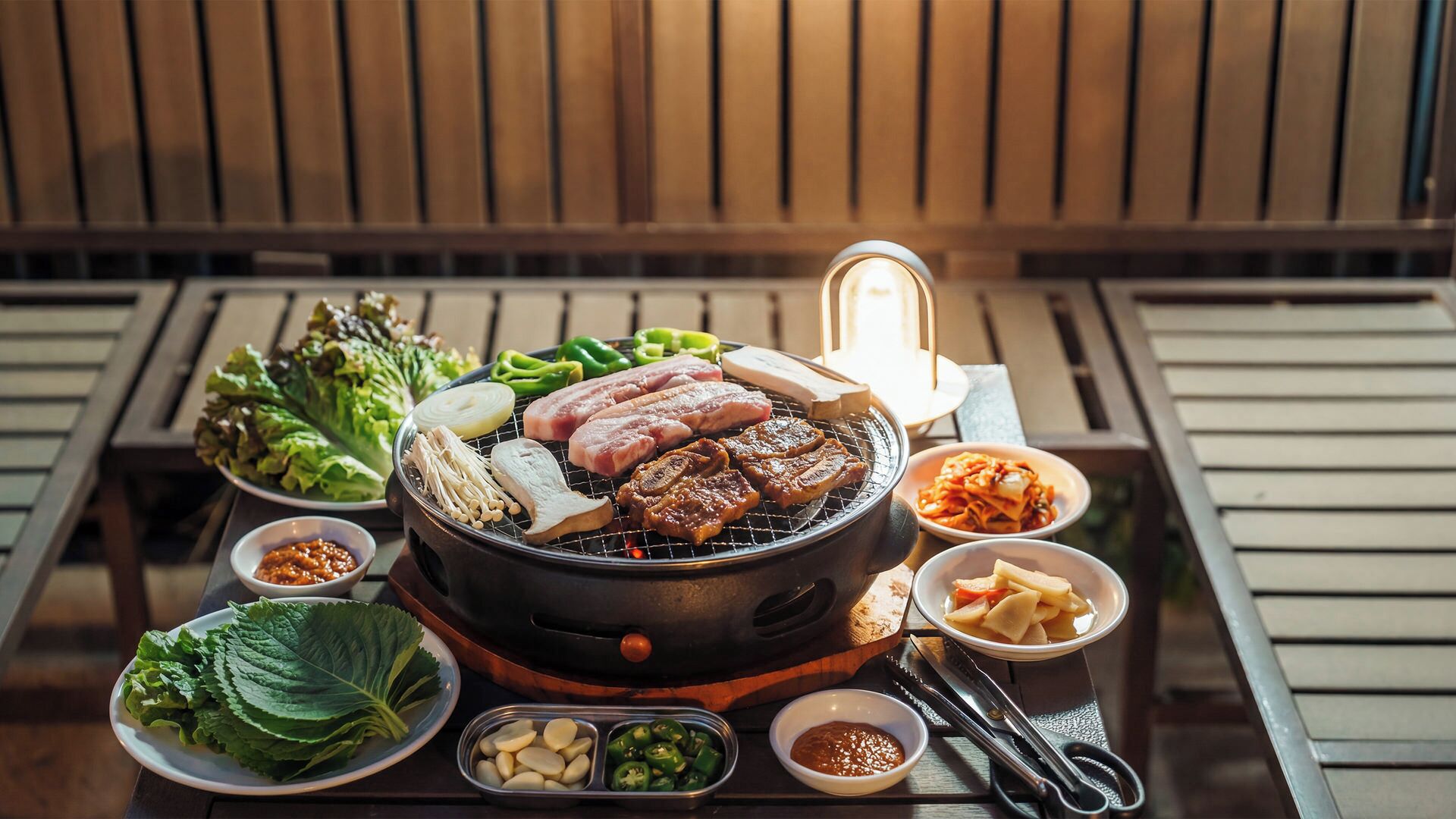 A grill with various meats and vegetables, a bowl of kimchi, and a plate of lettuce.