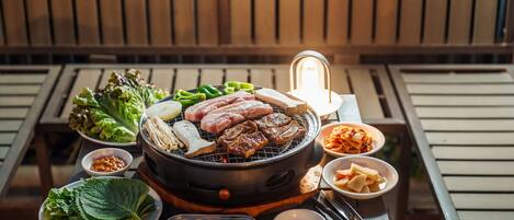 A grill with various meats and vegetables, accompanied by side dishes and condiments.