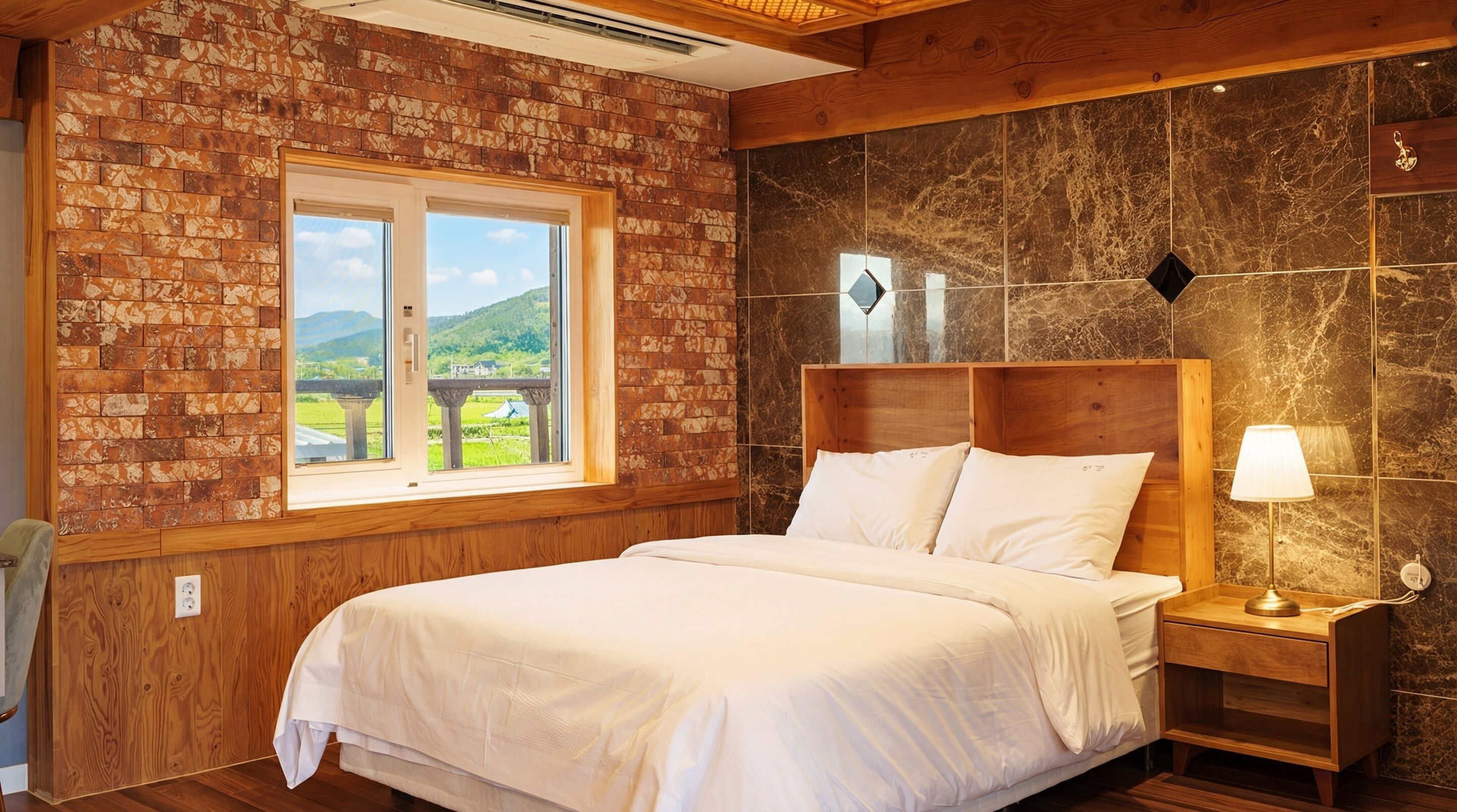 Un dormitorio con pared de ladrillo, un ventanal con vistas a zonas verdes, cabecero de madera y una lámpara de noche.
