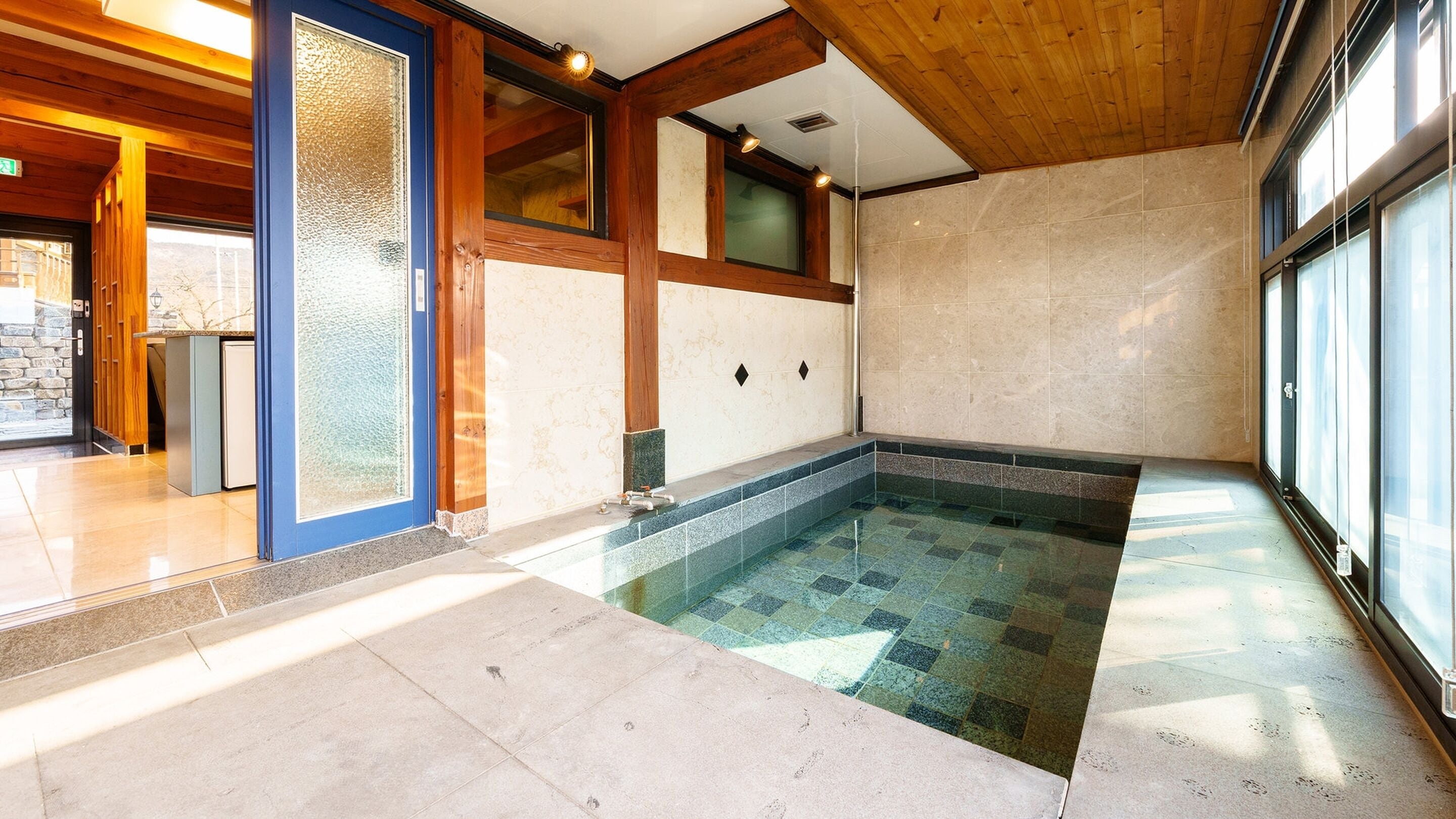 Ein moderner, überdachter Pool mit Steinfliesen, Holzbalken und großen Fenstern.