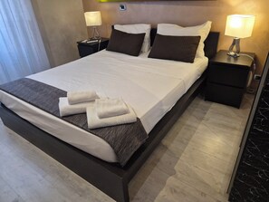 A neatly made bed with white linens, two bedside tables with lamps, and a set of towels on the bed.