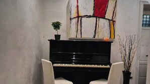 Un piano con dos sillas frente a él, una planta sobre el piano y un cuadro en la pared.