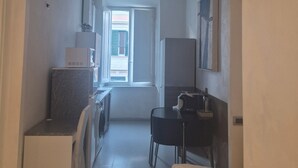 Ein schmaler Flur führt zu einer Küche mit Fenster, einer Waschmaschine und einem Essbereich mit Tisch und Stühlen.