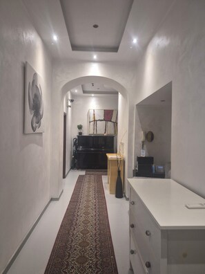 A hallway with a patterned rug, a black piano, a wooden cabinet, and a white dresser.