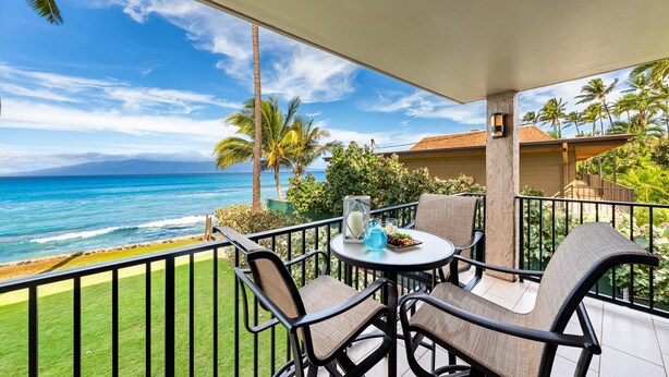 Een balkon met uitzicht op de oceaan, voorzien van stoelen en een tafel, en een klein decoratief object op de tafel.
