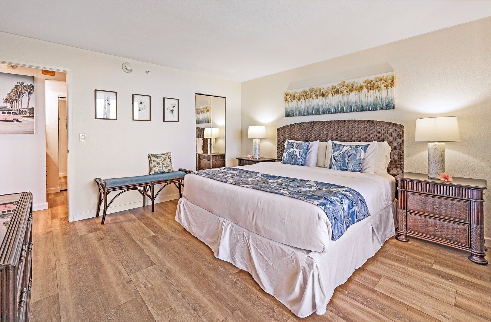 Quarto com cama grande, um banco, mesa de cabeceira e criado-mudo.