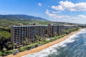Un hôtel à étages, situé en bord de mer, avec une vue sur les montagnes en arrière-plan.