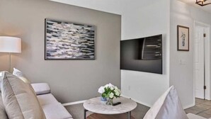 Ein modernes Wohnzimmer mit einer Couch, einem Couchtisch mit Blumenvase, einem Bild an der Wand und einem Flachbildfernseher über der Couch.