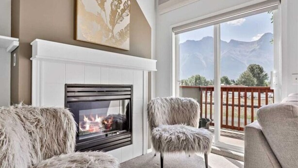 Ein Wohnzimmer mit Kamin, zwei fellüberzogenen Sessel und einem großen Fenster mit Blick auf die Berge.