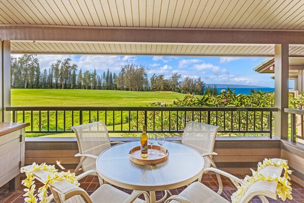 Uma área de estar coberta ao ar livre com vista para um campo de golfe e oceano.