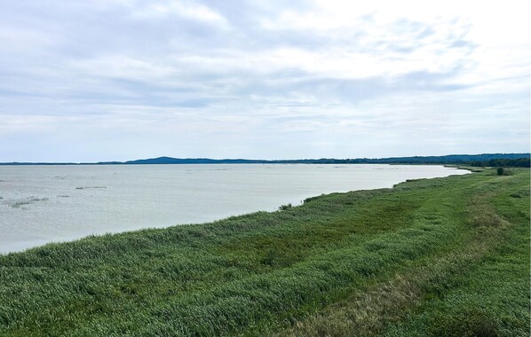 A coastal landscape with a grassy shoreline and a calm body of water extending to the horizon.
