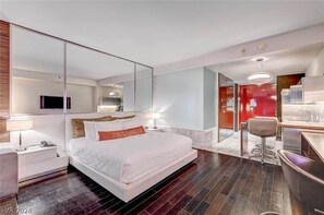 A modern hotel room with a large bed, a desk with a chair, a mirror, and a kitchenette. - Stunning Strip-view Studio w/ Balcony Access 35308 (Las Vegas)