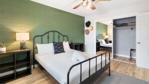 Una camera da letto con parete in mattoni verdi, un letto con biancheria bianca, un comodino con una lampada e una ventola a soffitto.