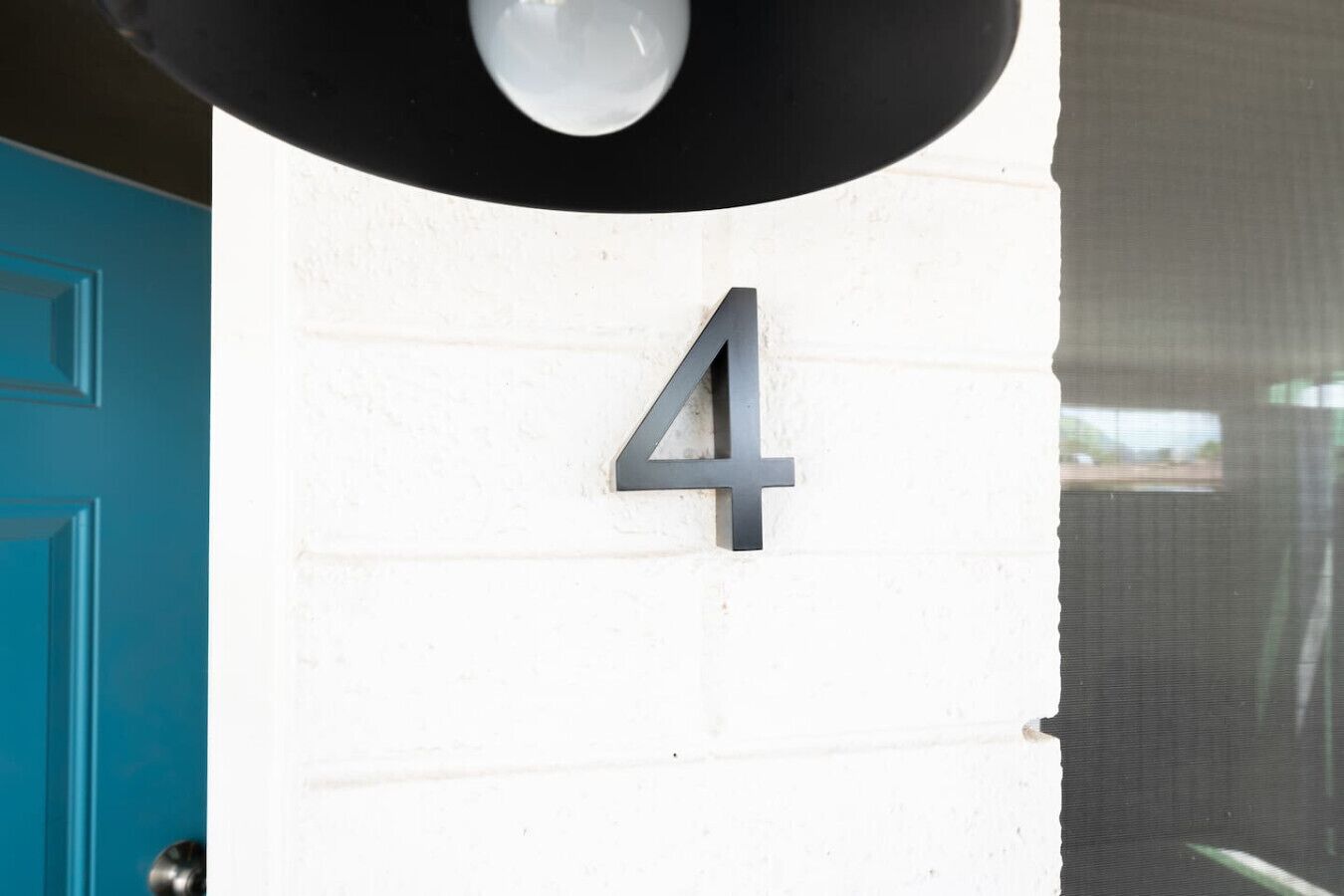 A house number '4' mounted on a white brick wall.