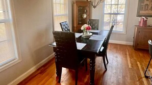 Une salle à manger avec une table et des chaises en bois, un lustre et un buffet orné d’une horloge.