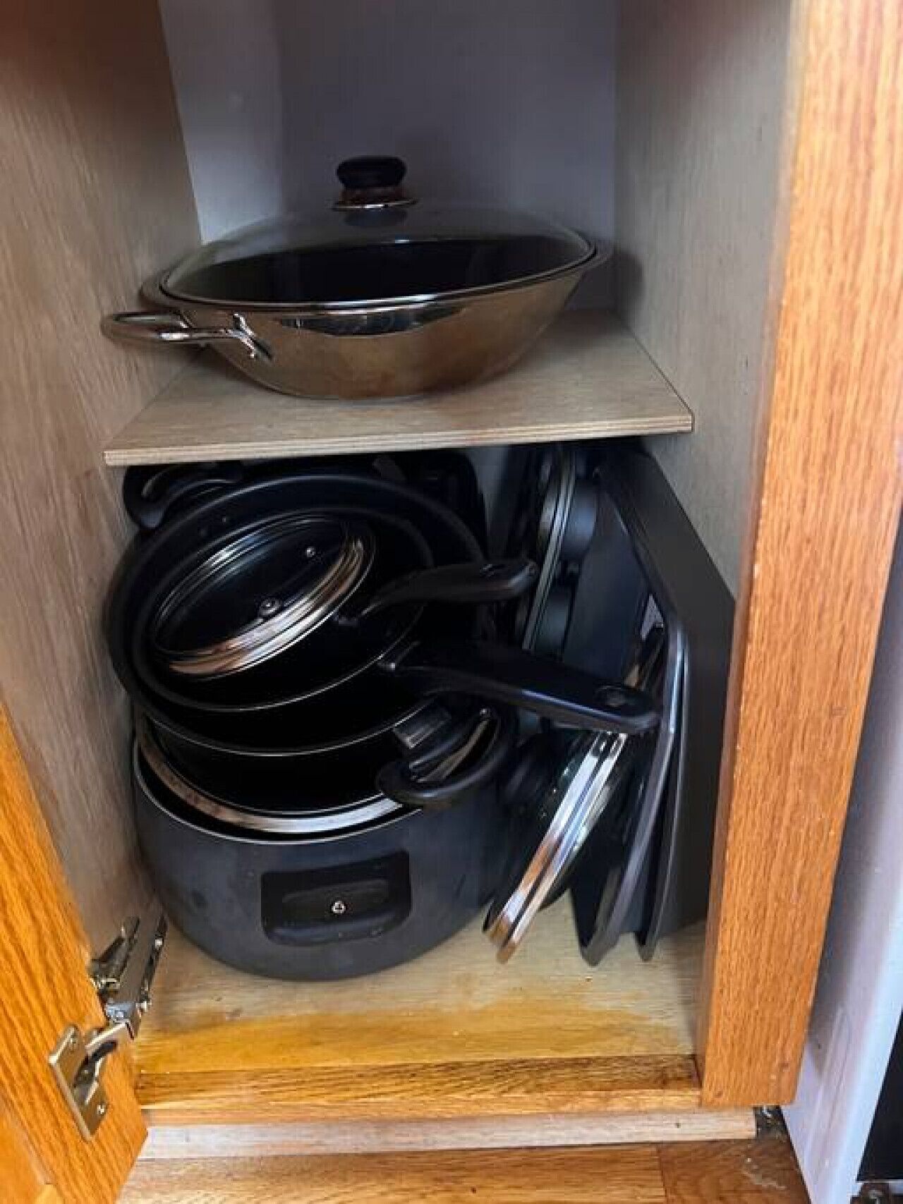A kitchen cabinet with a frying pan on the top shelf and several pots and pans below.