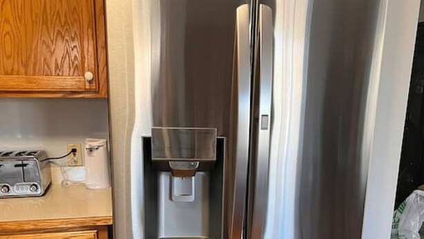 Un réfrigérateur en acier inoxydable doté d’un distributeur d’eau, situé dans une cuisine avec des armoires en bois et un plan de travail.