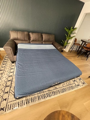 Ett rum med en brun lädersoffa, ett blått mönstrat överkast, en mönstrad matta, en krukväxt och ett litet matbord med stolar.