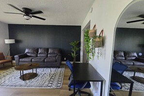 Un salon comprenant un canapé, une table basse et des fauteuils, un ventilateur de plafond et une plante.