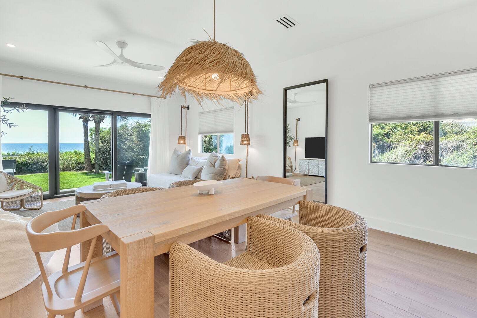 Un espace de repas moderne avec une table en bois, des chaises en osier et une grande fenêtre donnant sur l’extérieur.