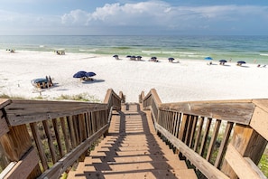 Una escalera de madera que conduce a una playa de arena blanca y agua azul cristalina.