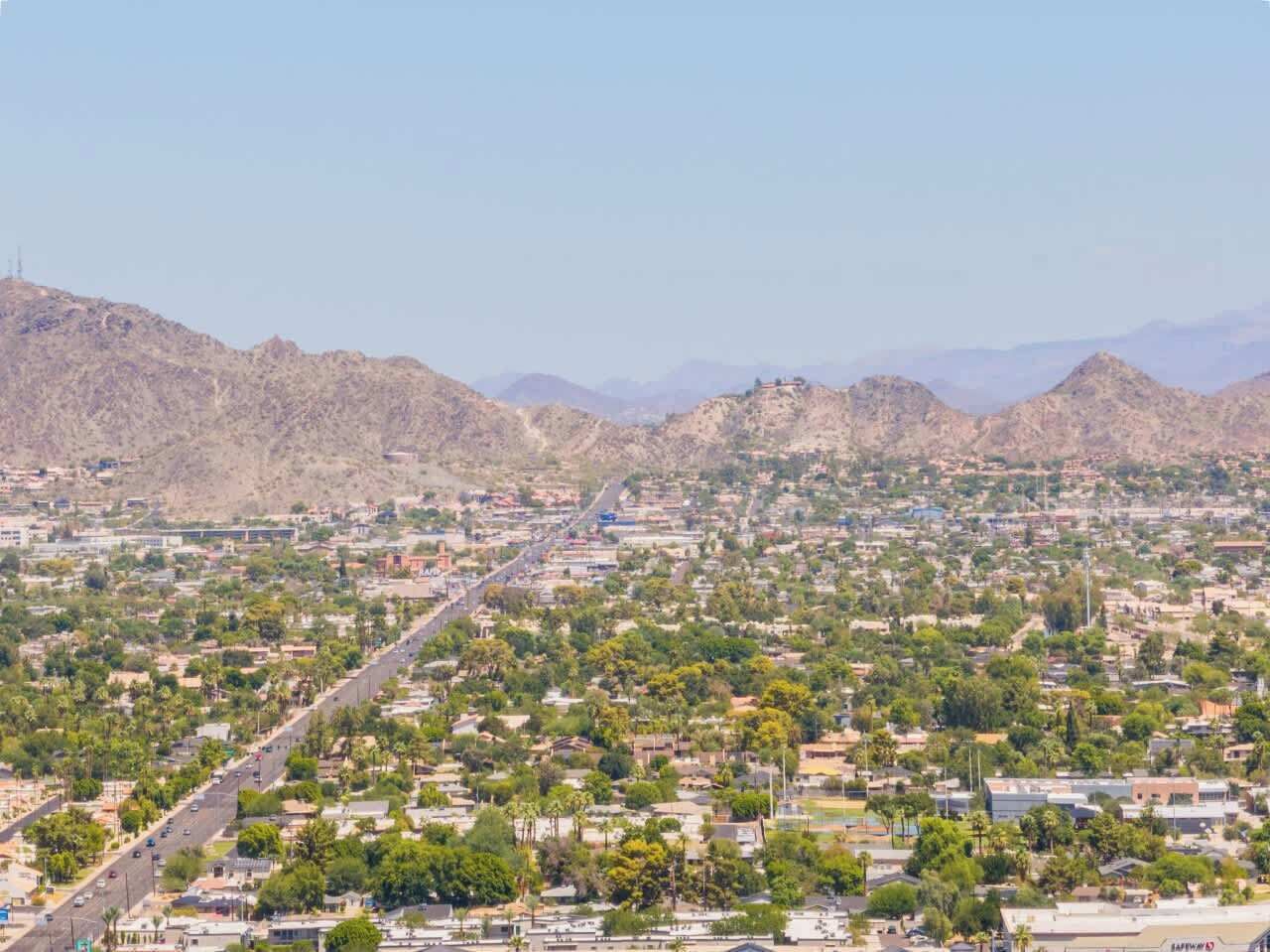 A cityscape with a prominent road running through it, surrounded by residential areas and hills in the background.