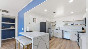 A modern kitchen with white cabinetry, a marble island, and a blue accent wall. - New! Blue&pink Pool Centra PHX (Phoenix)