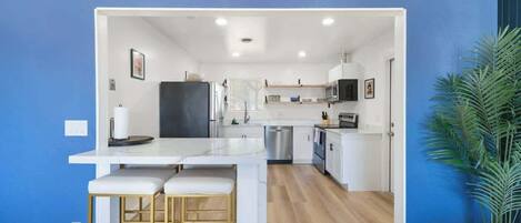 Una cocina moderna con armarios blancos, un refrigerador de acero inoxidable y una mesa de madera con dos sillas.