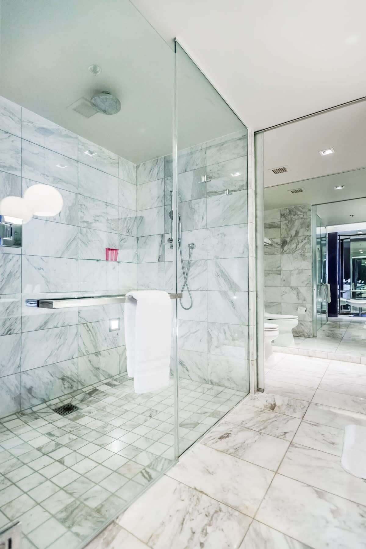 Une salle de bain moderne avec des carreaux de marbre, une douche en verre et des toilettes apparentes.