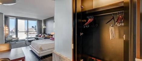 Habitación de hotel moderna con una cama grande, un escritorio y vistas a la ciudad. Hay una zona separada con perchero y ropa colgada.