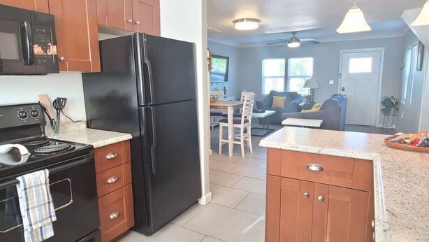 A kitchen with a black refrigerator, wooden cabinets, a stove, and a microwave. There is a dining area with a table and chairs in the background. - Charming Apt Downtown Phoenix Historic Patio (Phoenix)