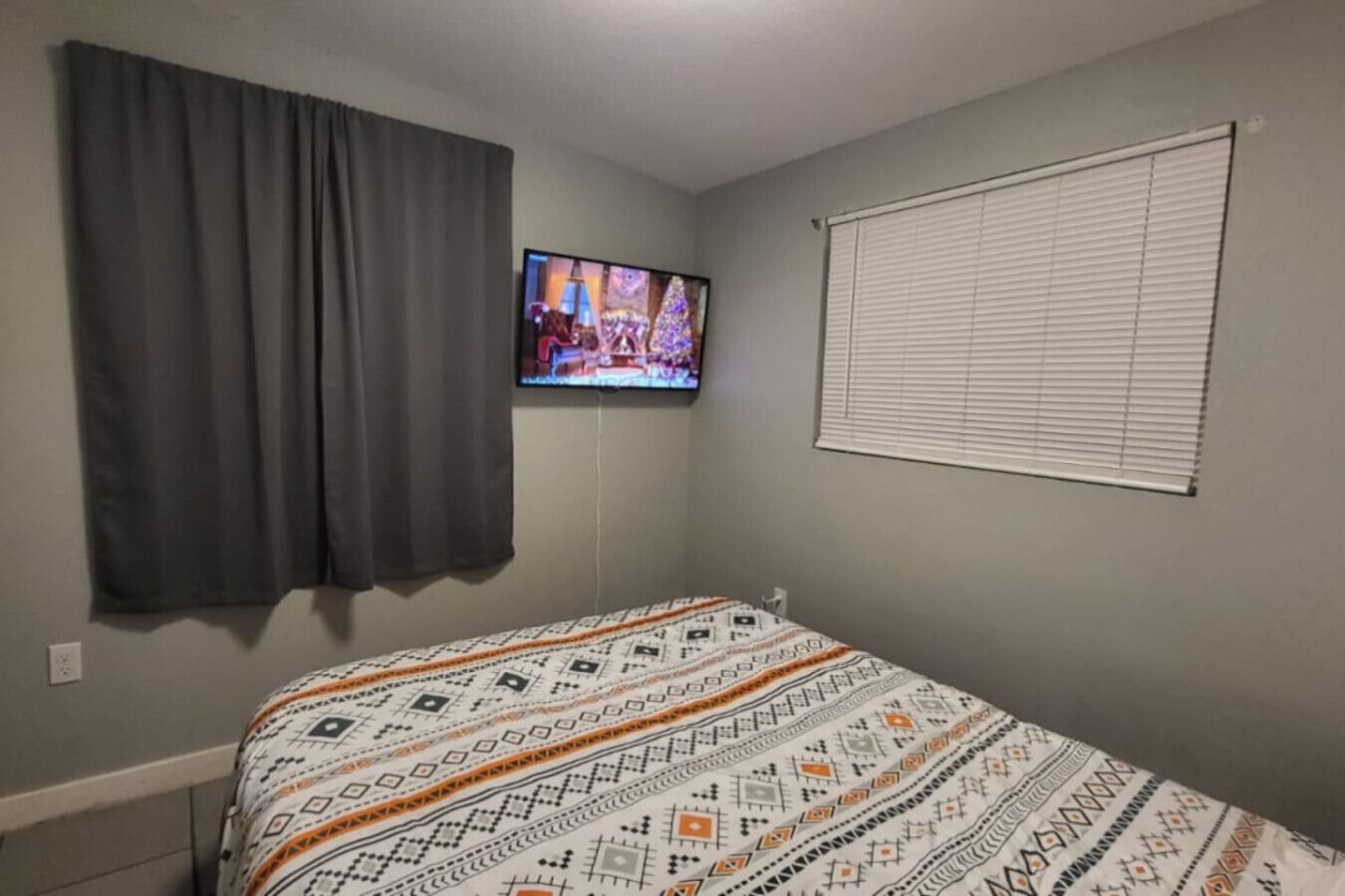 Une chambre à coucher avec un lit, un téléviseur fixé au mur et une fenêtre avec des stores.