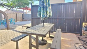 A patio with a wooden table and benches, a blue umbrella, and a wooden fence in the background. - Charming Apt Downtown Phoenix Historic Patio (Phoenix)