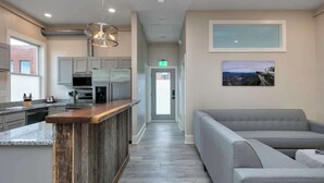A modern kitchen with a wooden bar, grey upholstered seating, and a hallway leading to a door. - Light-filled Adventure Loft (Roanoke)