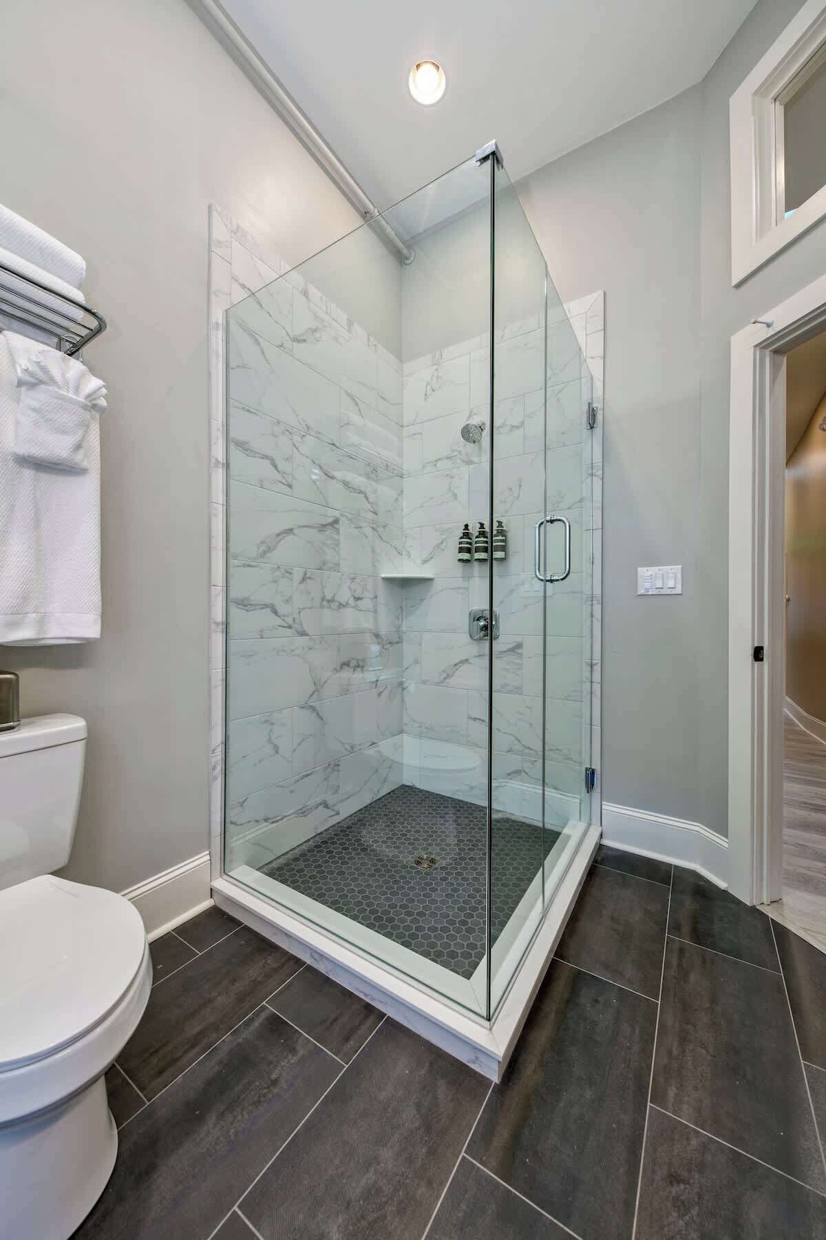 Een moderne badkamer met een douchecabine van glas, marmeren tegels en een donkere vloer.