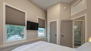 A bedroom with a bed, a TV mounted on the wall, and a door leading to a bathroom. - Light-filled Adventure Loft (Roanoke)