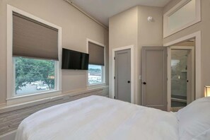 Une chambre à coucher comprenant un lit, une télévision, une fenêtre avec des stores et une porte donnant sur une salle de bain.