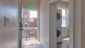 A laundry room with a washing machine and dryer, a door leading to a balcony with a chair, and a visible exit sign. - Light-filled Adventure Loft (Roanoke)