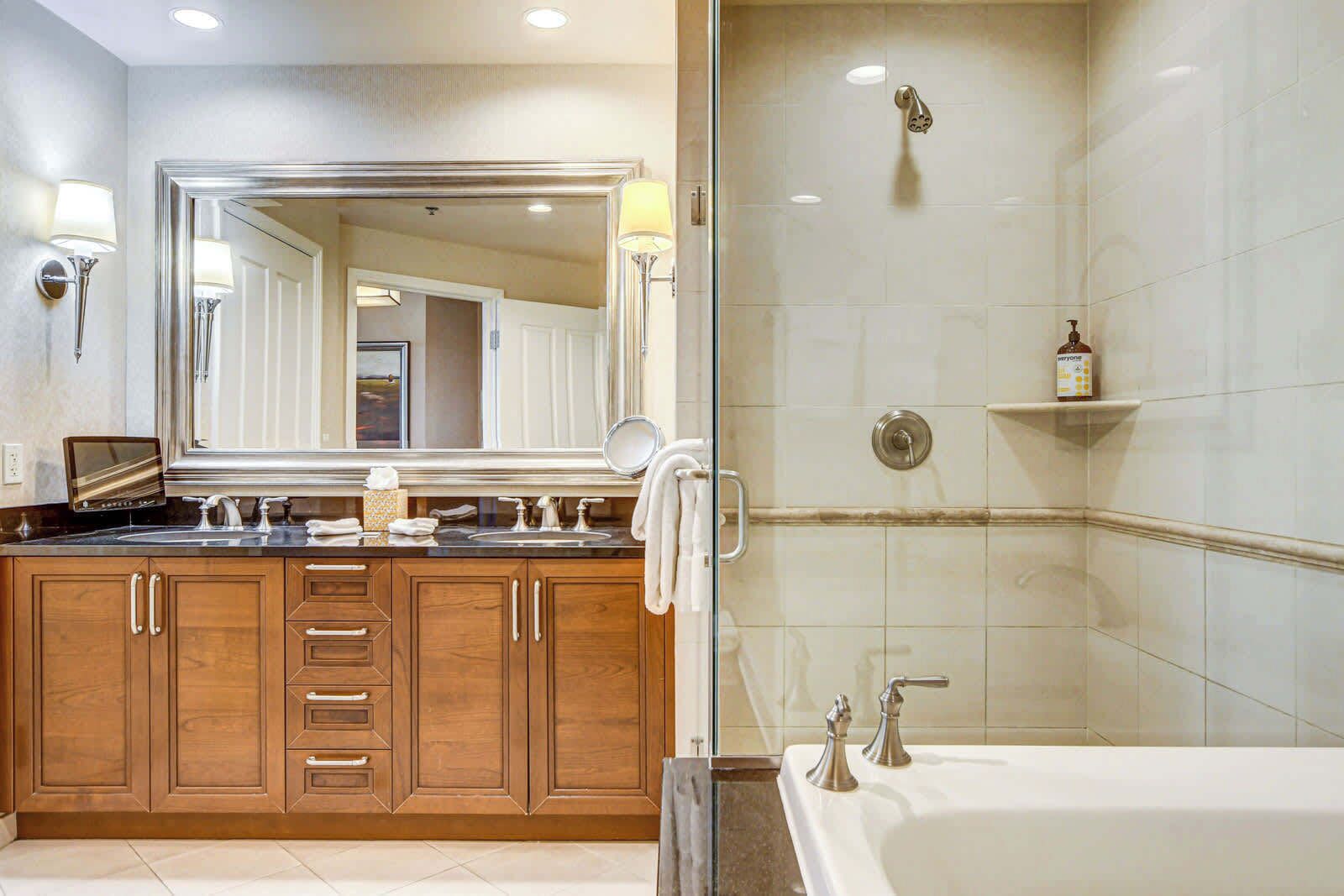 Un baño moderno con un espejo grande, armarios de madera, una bañera y zona de ducha.