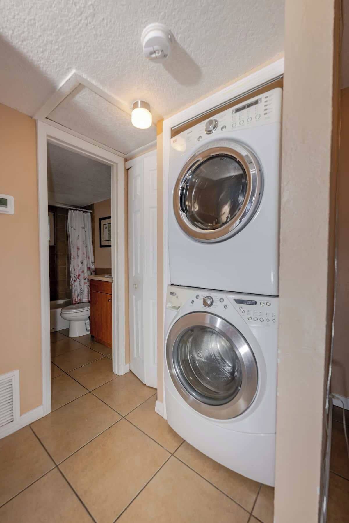 A laundry room with two stacked front-loading washing machines, a toilet, and a shower area.