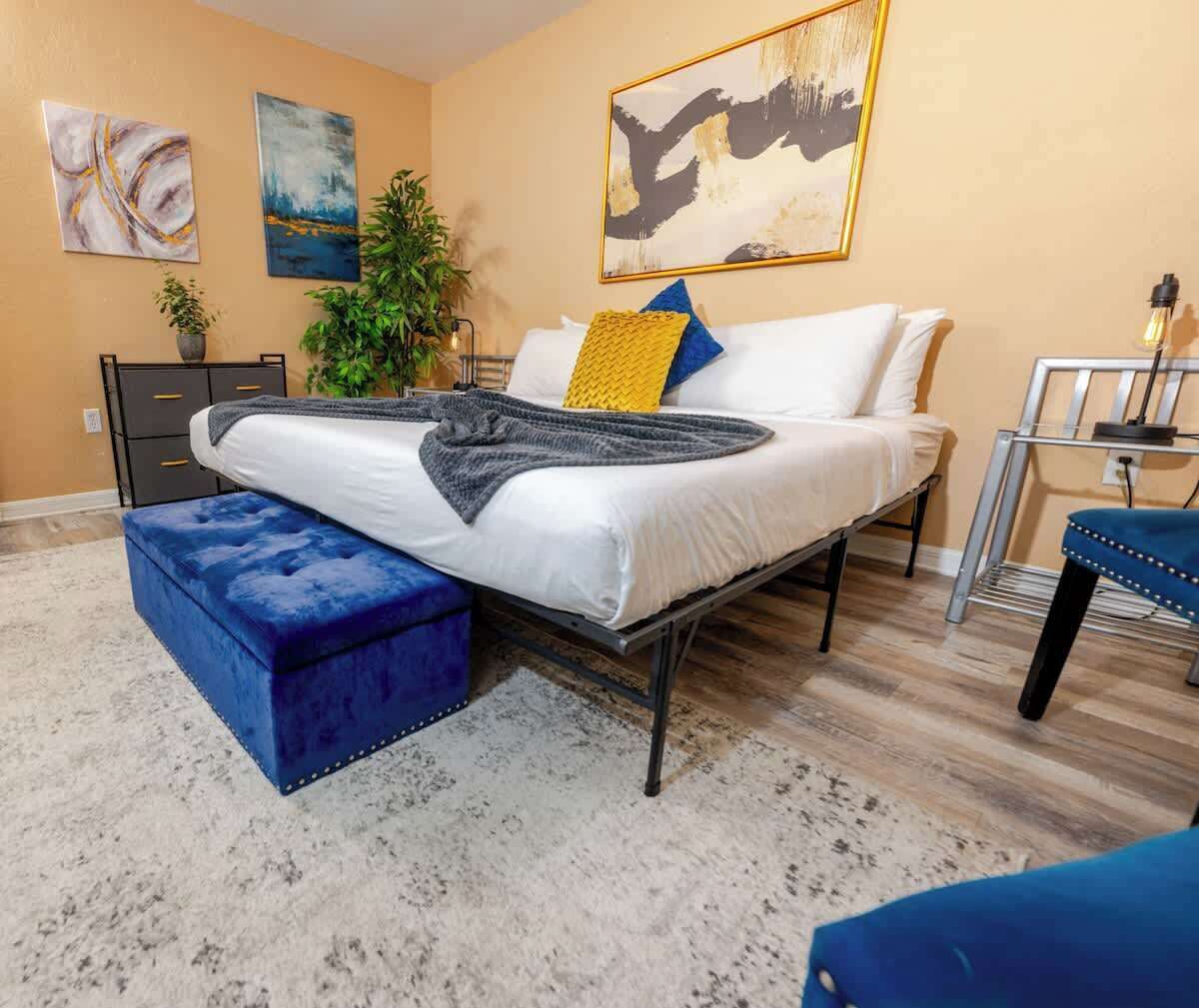 Un dormitorio con una cama, un reposapiés azul, un escritorio y una silla.