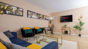 Una sala de estar con sofá, sillones, una mesa de centro, televisor y obras de arte en la pared.