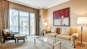 A hotel room with a sofa, armchair, and ottoman, a glass coffee table, a floor lamp, and a large window with curtains. - Large 1BR at MGM With Strip View (Las Vegas)
